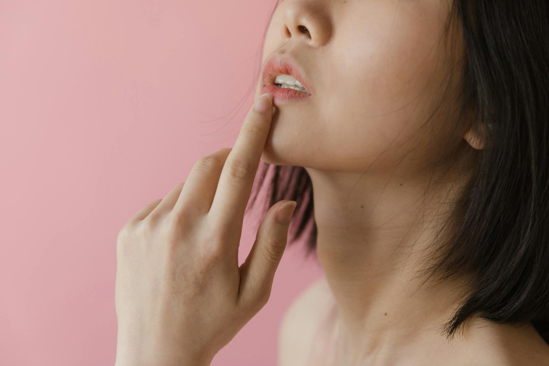 Kobieta z niepokojem dotyka ust na różowym tle